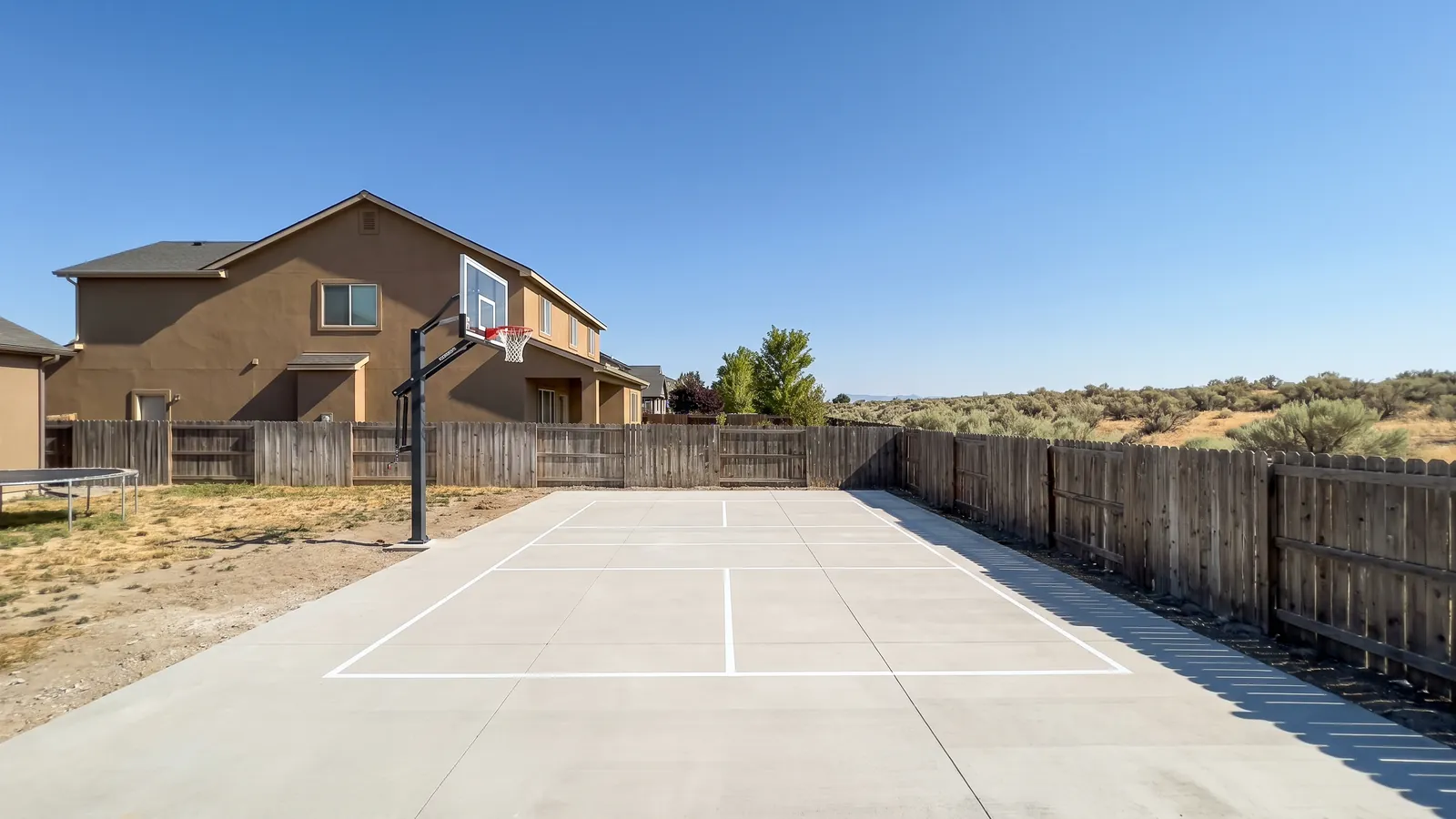 Newly poured backyard concrete sport court with a basketball hoop behind a two-story home in a Meridian, Idaho subdivision